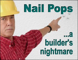 builder in bright yellow hard hat points to disfiguring  dry wall nail pops on wood-framed wall